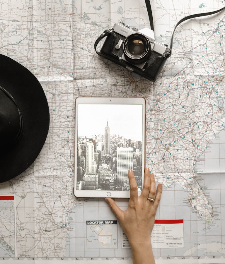 Person Touching Silver Ipad on World Map Chart Beside Black Hat