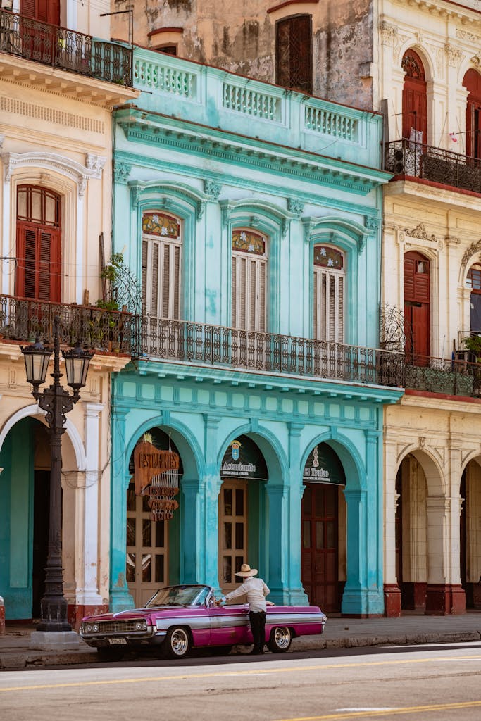 Man Standing beside His Car in front of Colorful Buildings in Havana, Cuba