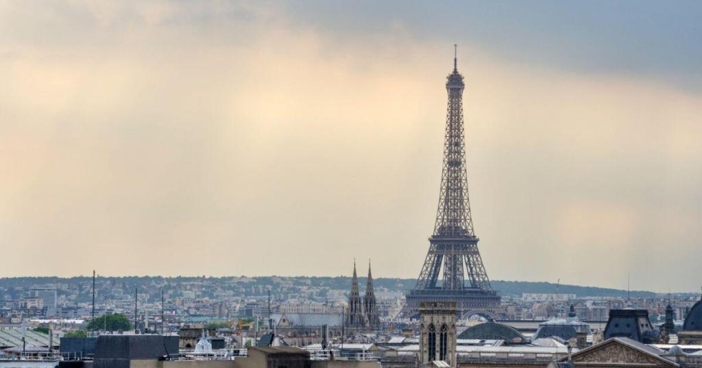 View of the Eiffel Tower under a cloudy sky, embraced by the charming Parisian cityscape with distant buildings and rooftops.