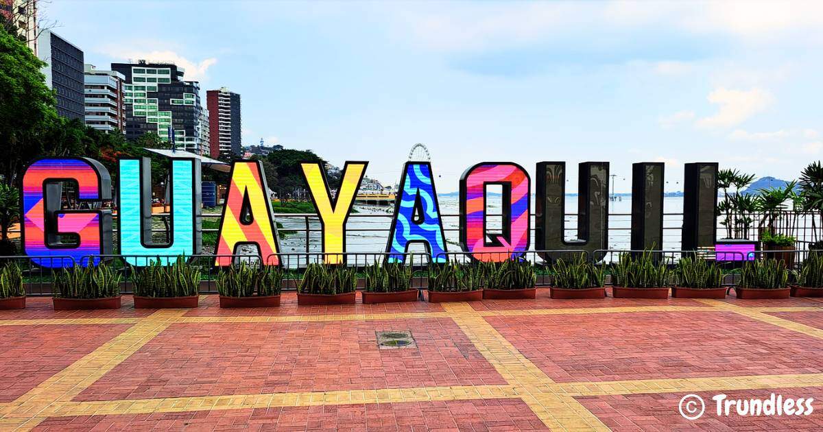 Colorful "Guayaquil" sign with buildings and a Ferris wheel in the background, surrounded by plants and a brick walkway in the foreground.