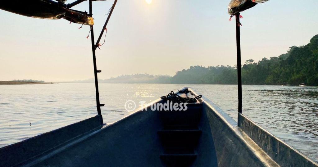 A boat on a calm river with a view of distant trees under a hazy sky.