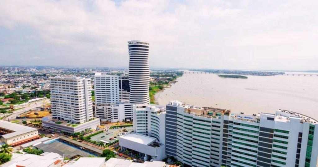 Aerial view of a cityscape with modern high-rise buildings near a large body of water under a cloudy sky.