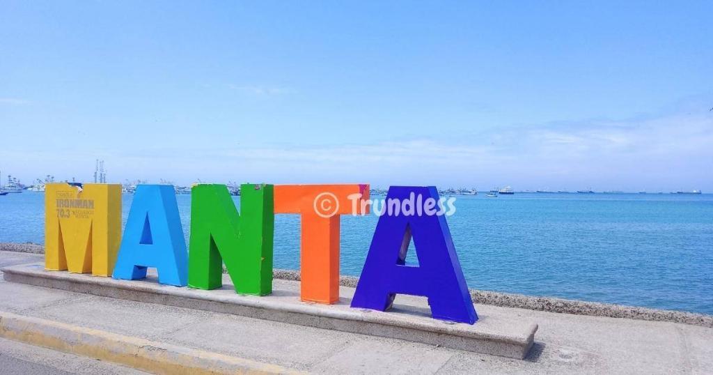 A colorful "MANTA" sign by the ocean, with a blue sky and distant ships elegantly framing the scene.