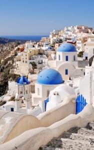 Scenic view of a coastal village with white buildings and blue domes in Santorini, Greece, overlooking the sea.