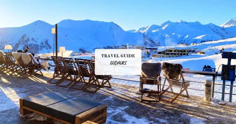 Wooden deck chairs with fur coverings on a snowy mountain overlook, under a clear blue sky in Gudauri.