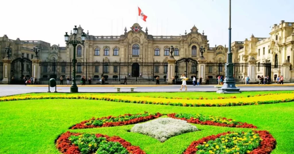 Front view of the Government Palace of Peru in Lima, with a well-maintained garden and a flag on top.