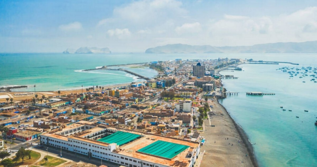 Aerial view of a coastal city with shoreline buildings, a pier, and distant islands.