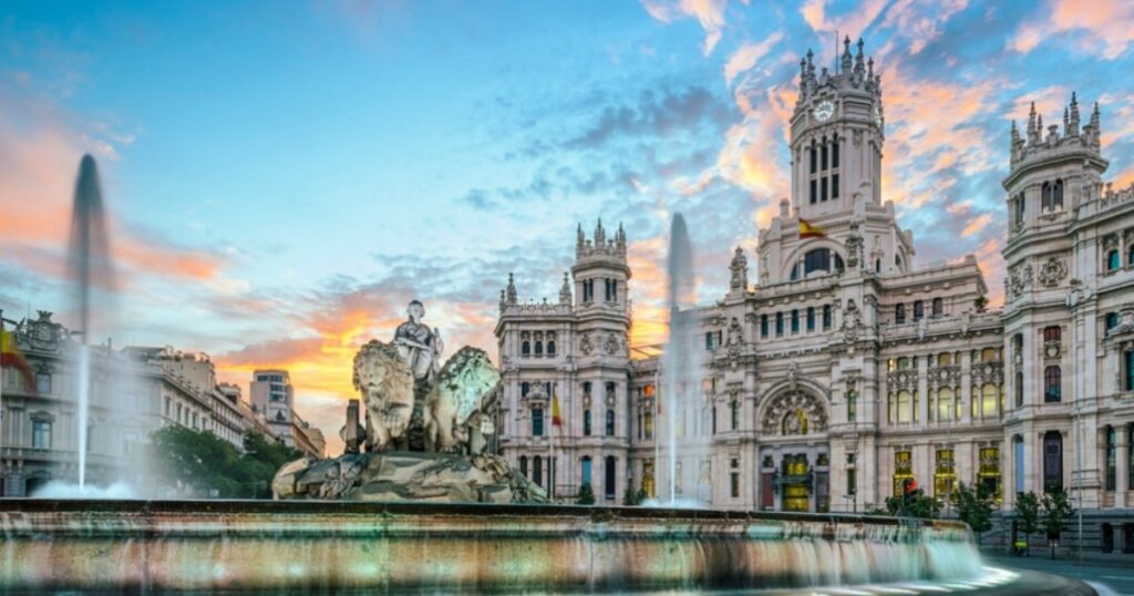 Cibeles Fountain and statue with lions before Palacio de Cibeles in Madrid at sunset, water jets rising.