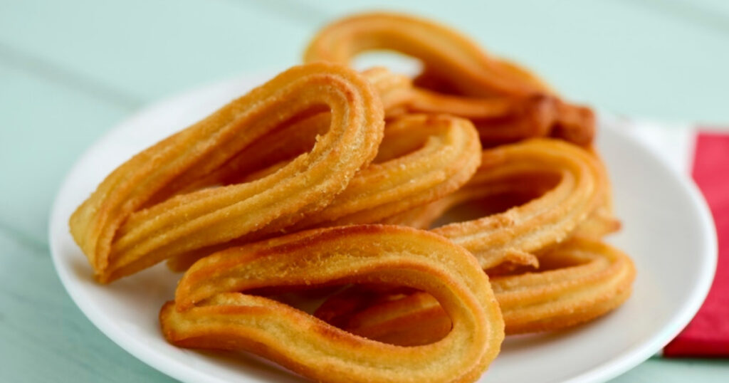 Golden-brown churros on a white plate, light blue surface, and a red napkin at the side.