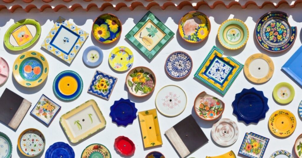 Colorful ceramic plates with different shapes and patterns hang decoratively on a white outdoor wall.